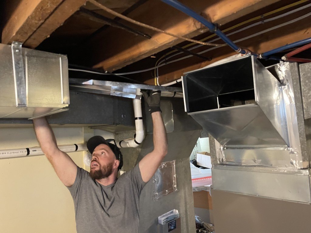 Technician fitting a sheet metal supply duct overhead