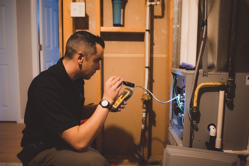 Technician holding a combustion analyzer at the burner compartment of a gas furnace