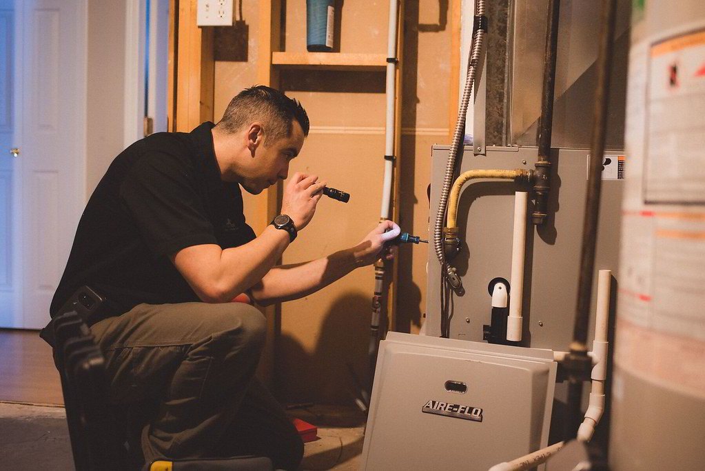 Technician with a flashlight checking a furnace in a hall closet