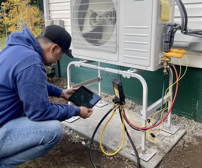 Technician reading system pressures on a tablet beside an outdoor heat pump unit