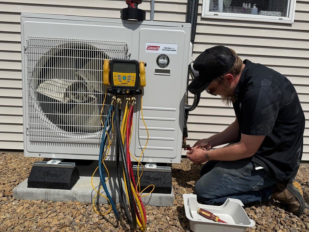 Technician commissioning a newly installed outdoor unit on a pad beside a house