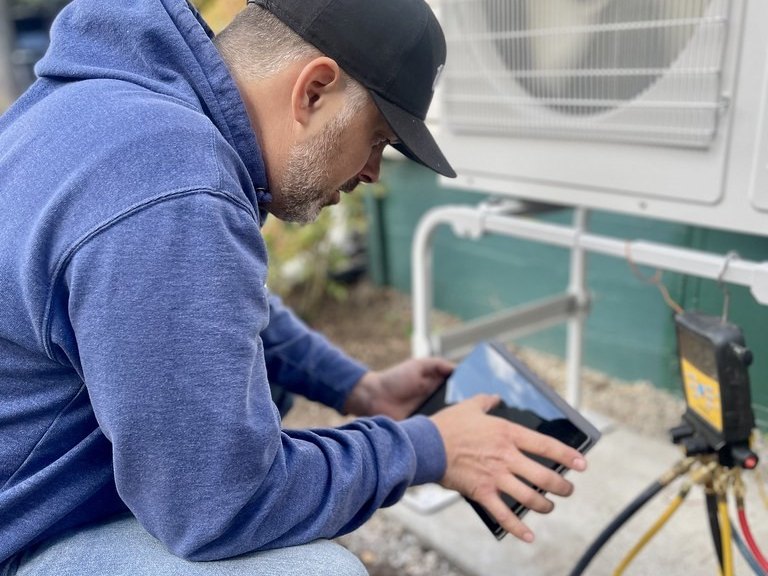 Technician checking refrigerant pressures on a tablet with gauges hooked to an outdoor unit